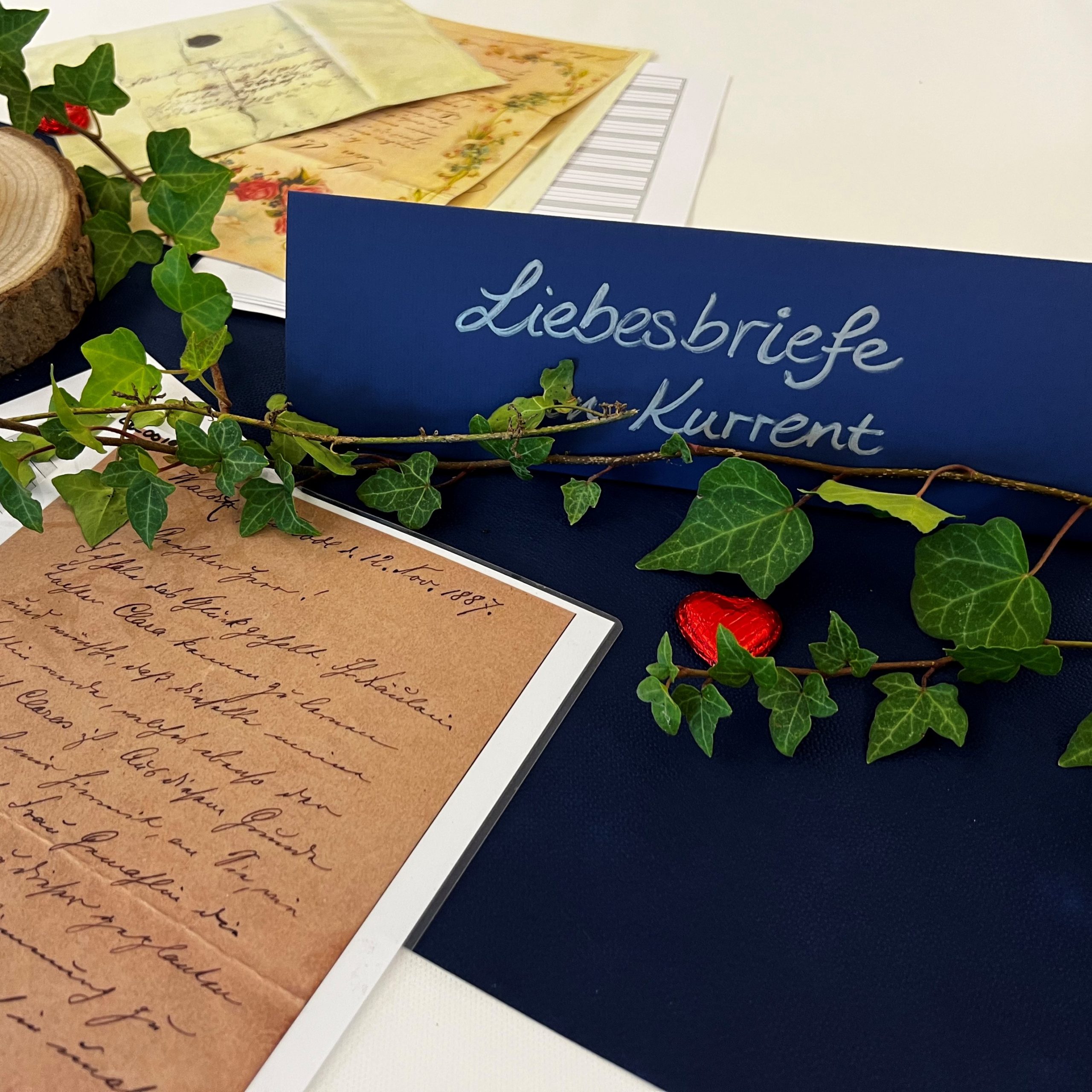 Der Thementisch zu Liebesbriefen in Kurrent mit rotem Schokoladenherz, umgeben von Efeu und Liebesbriefen