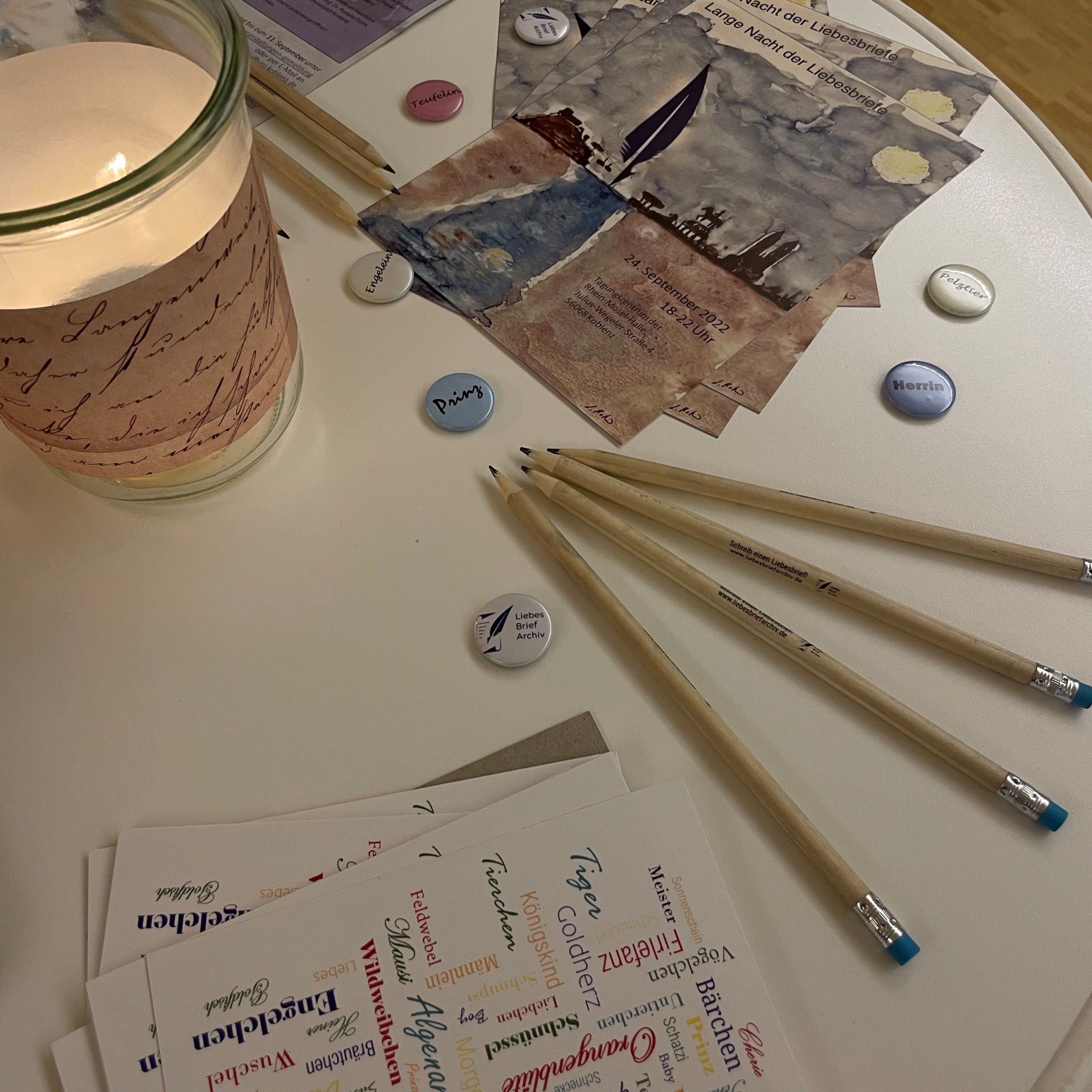 Kerze mit Postkarten, Lesezeichen, Bleistiften und Buttons mit Kosenamen des Liebesbriefarchivs