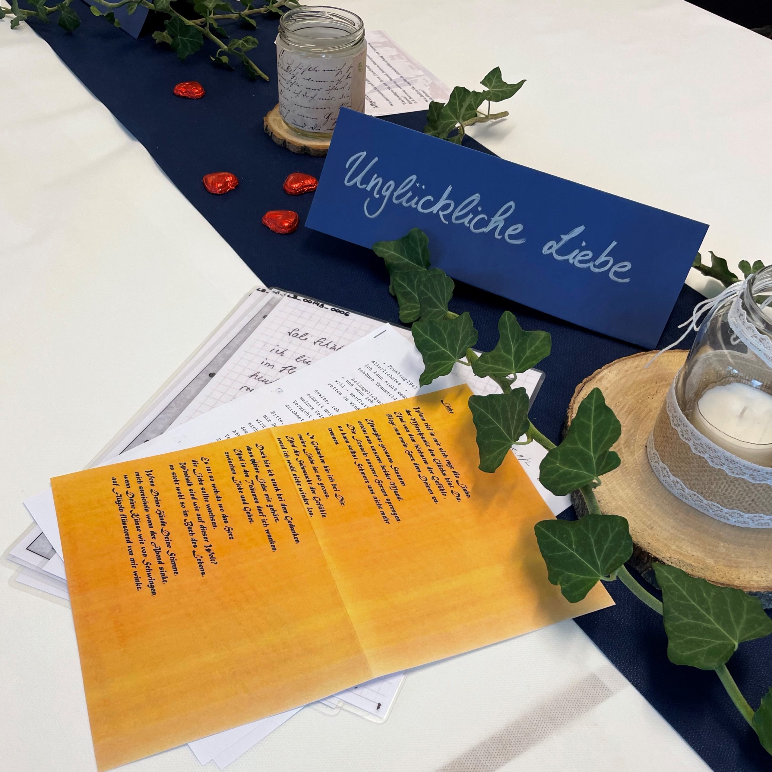 Der Thementisch zu unglücklicher Liebe mit Liebesbriefen, festlich dekoriert mit Efeu, Kerzen und Schokoladenherzen auf blauem Tischläufer