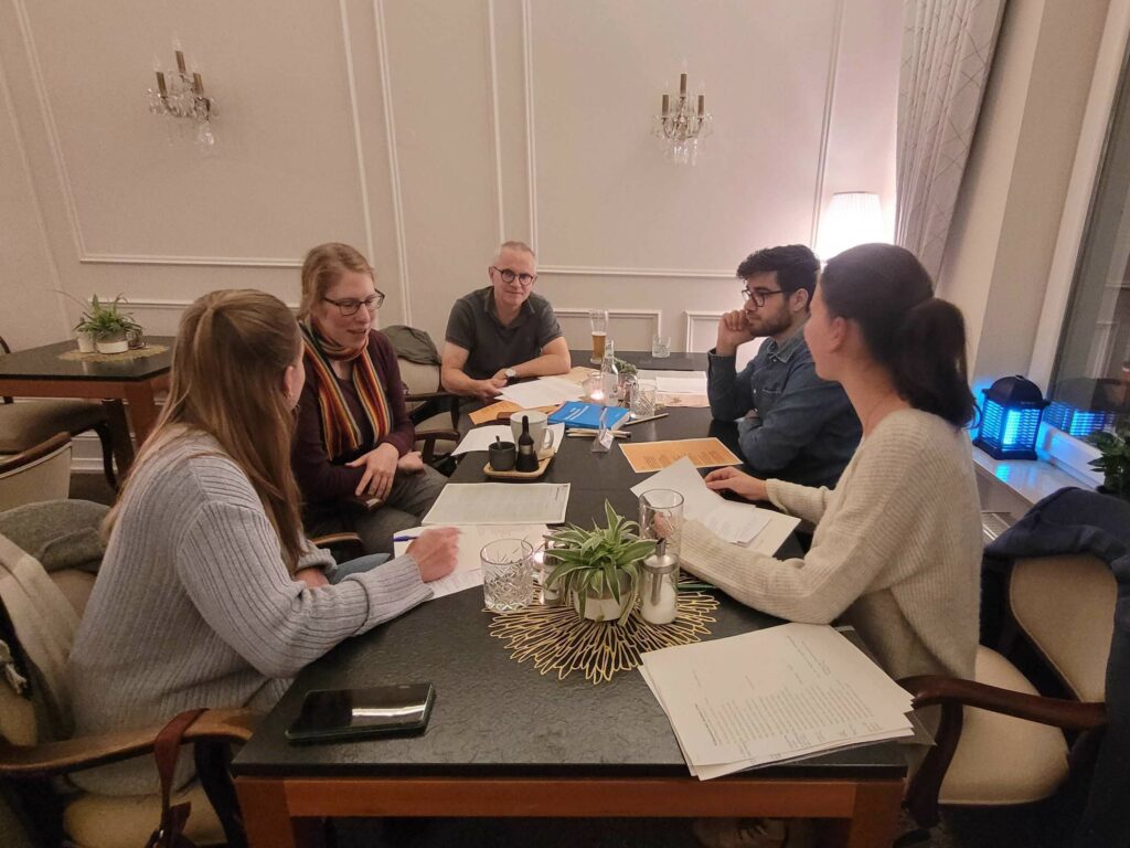 Citizen Scientists und eine Mitarbeiterin des "Gruß & Kuss"-Projekts sitzen mit Liebesbriefen und Getränken an einem Tisch im Kleinen Riesen in Koblenz